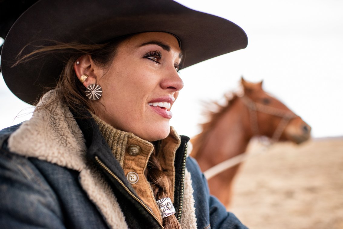 A cowgirl's face as she rides through a field with her horse.