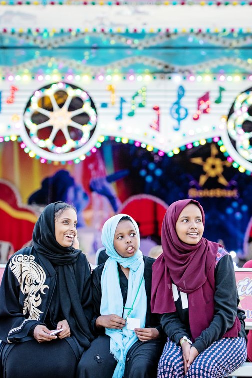Three muslim girls smiling on a bench at the fair in Rochester Mn